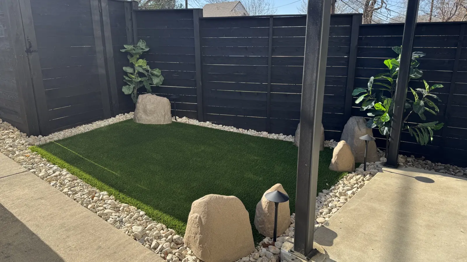 Artificial turf pet area framed with white river rocks and landscape lighting