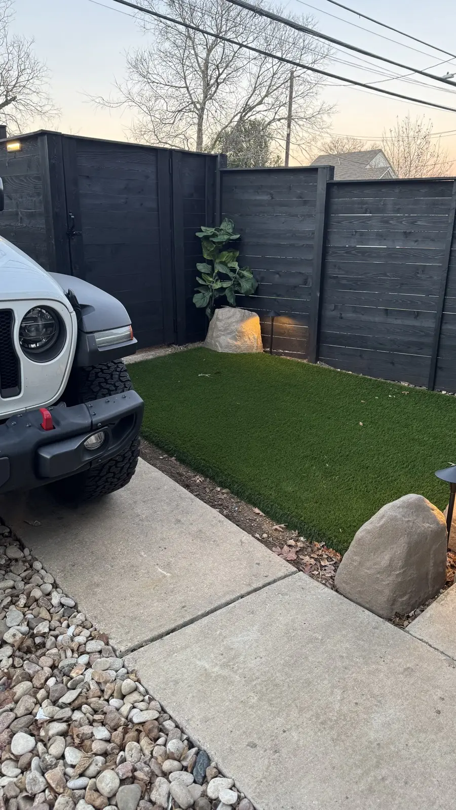 Finished backyard putting green at dusk with flags, rocks, and lit limestone steps