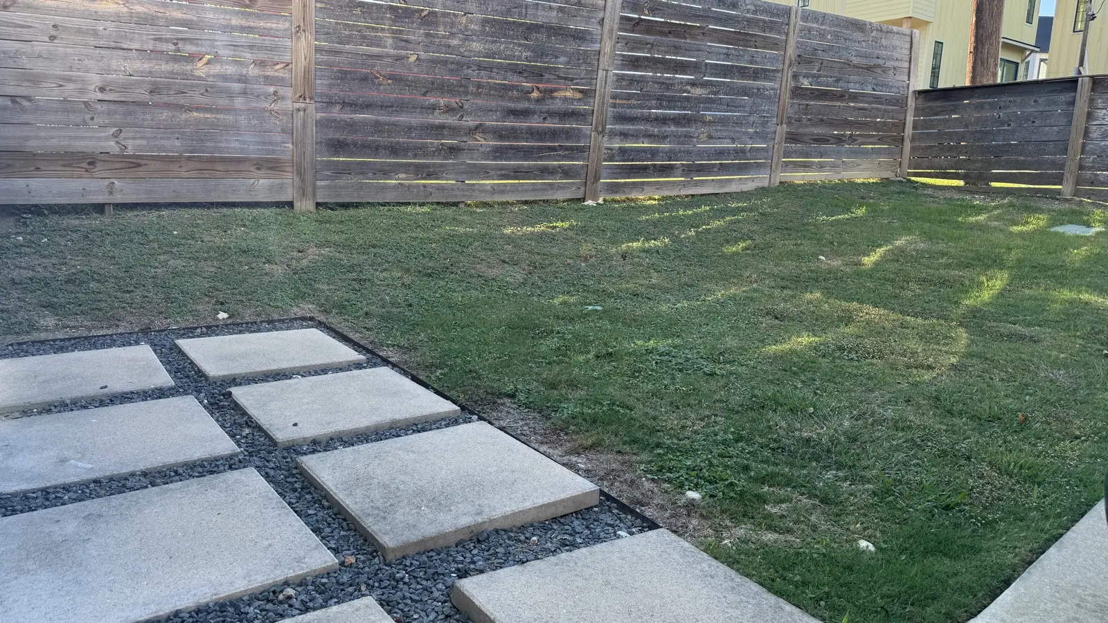 The backyard before installing artificial turf: patchy grass and bare pavers
