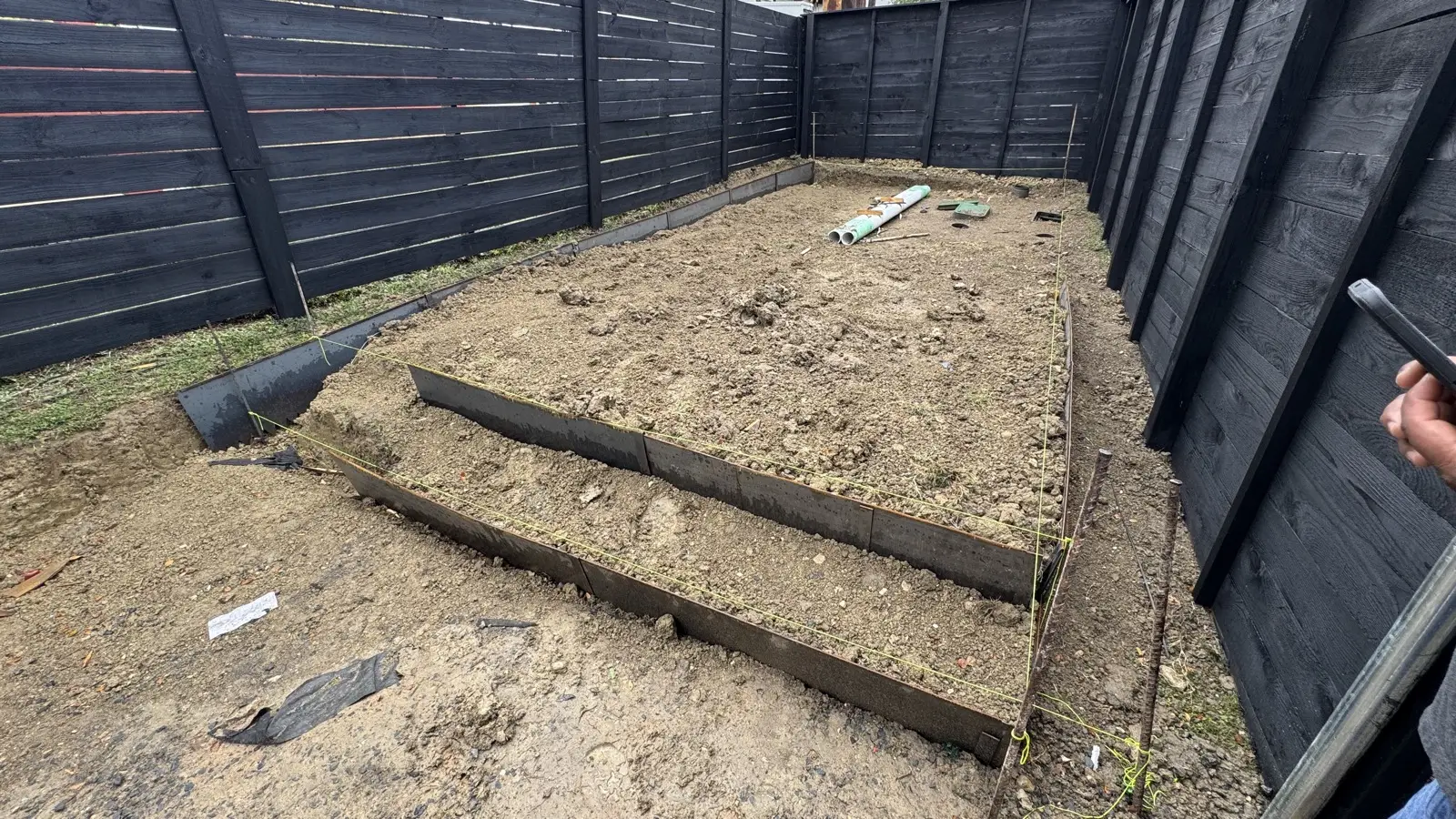 Graded and terraced dirt with retaining wall edging staked out for the putting green